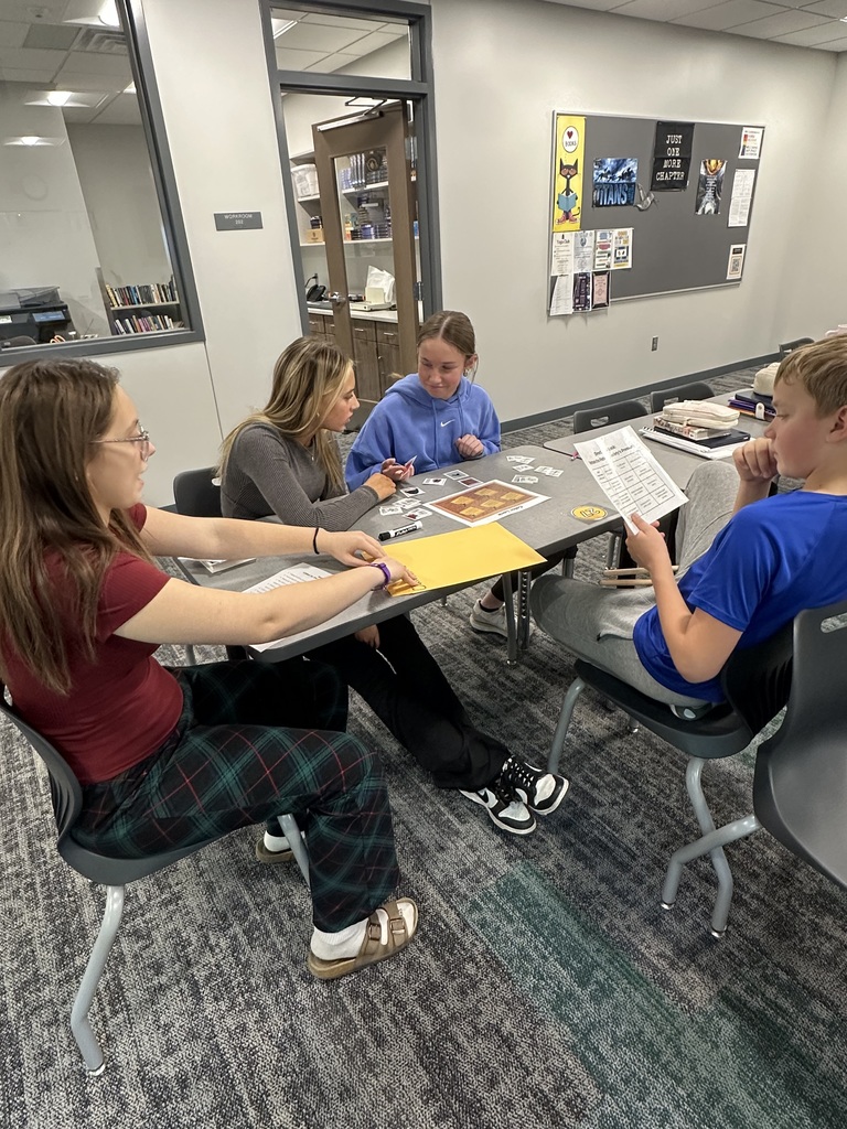 Four students sit at a table with various pieces of paper. They are all looking at the pages. 
