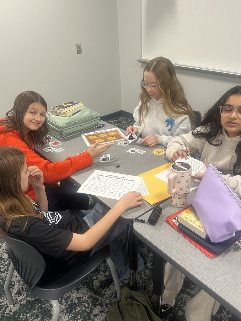 Four students sit at a table with various pieces of paper. They are all looking at the pages. 