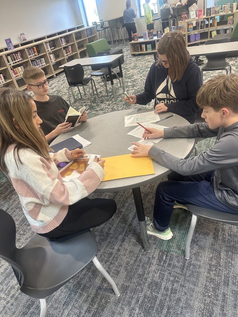 Four students sit at a table with various pieces of paper. They are all looking at the pages. 