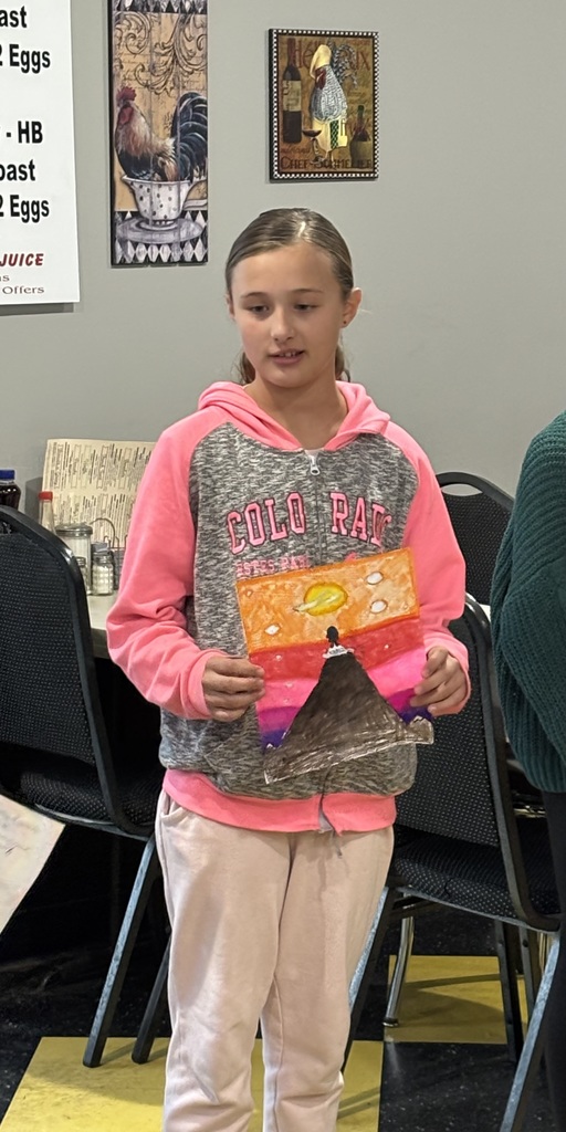 student holding their artwork of a person standing on top of a mounting looking at the sunrise