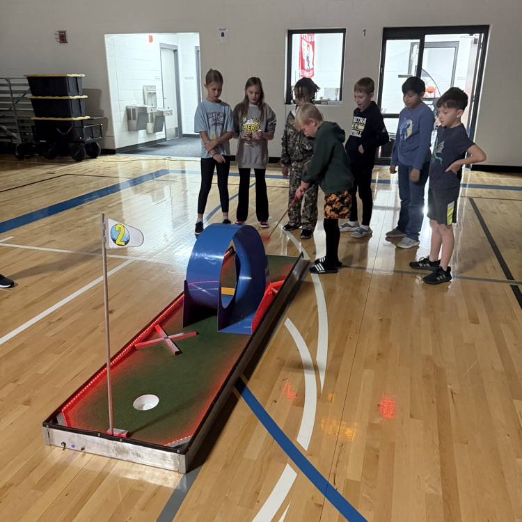 students watching a classmate hit a ball on a glow golf hole. 
