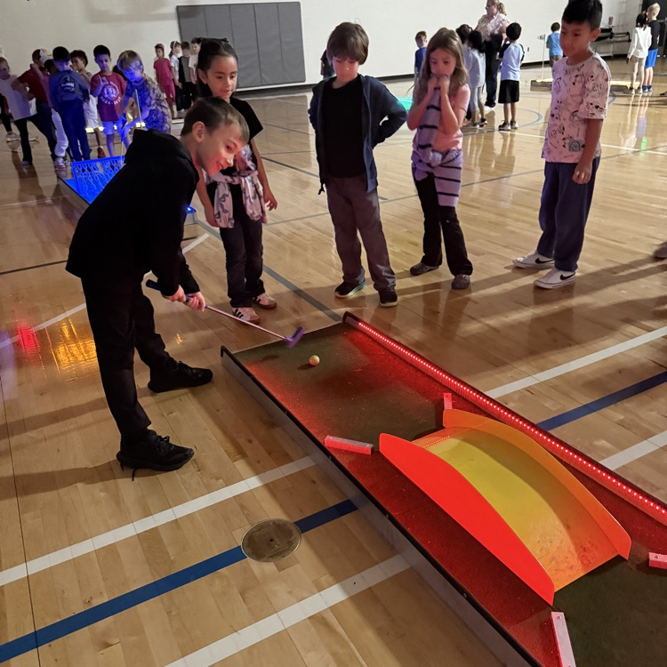 students watching a classmate hit a ball on a glow golf hole. 
