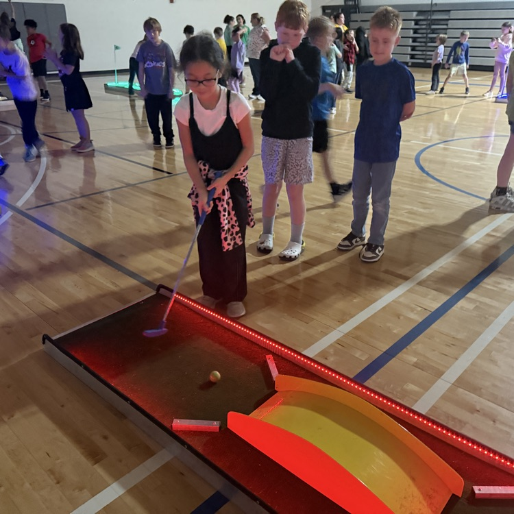 students watching a classmate hit a ball on a glow golf hole. 