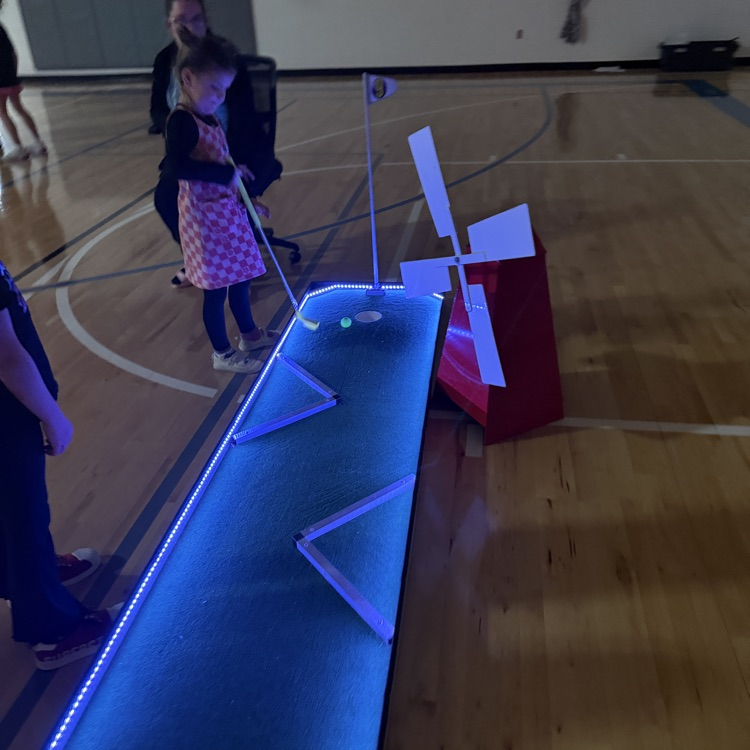 a kindergarten students hits a ball on a glow golf hole. 