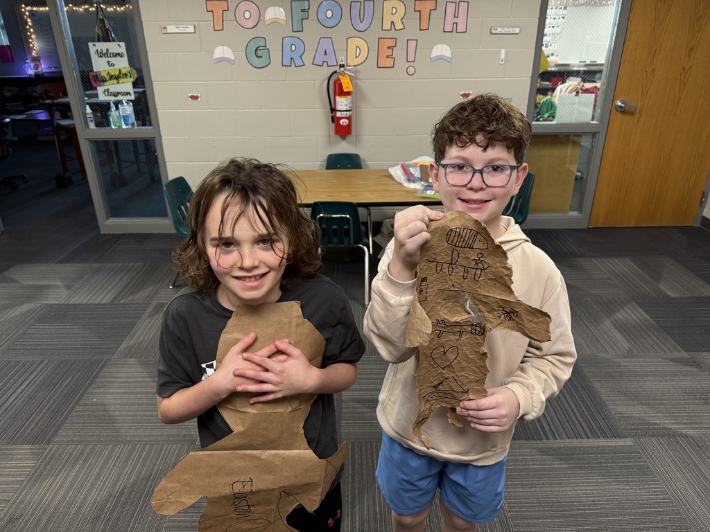 Two boys holding designs made out of paper bags with drawings on them that resemble buffalo hides.