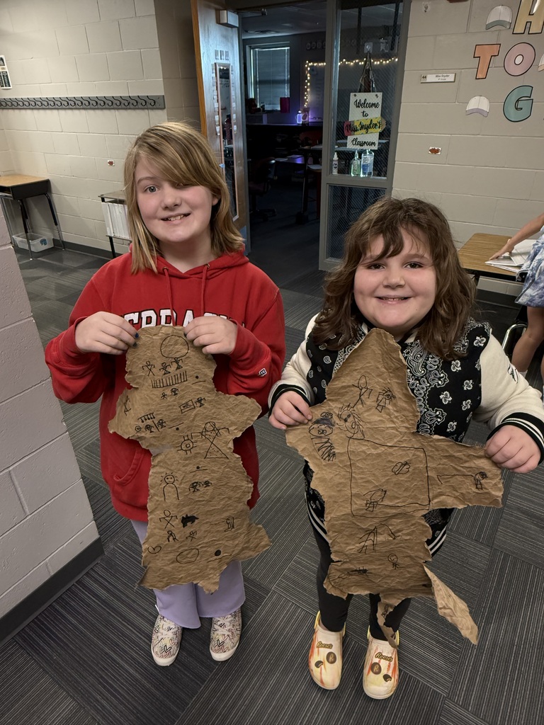 Two girls holding designs made out of paper bags with drawings on them that resemble buffalo hides.