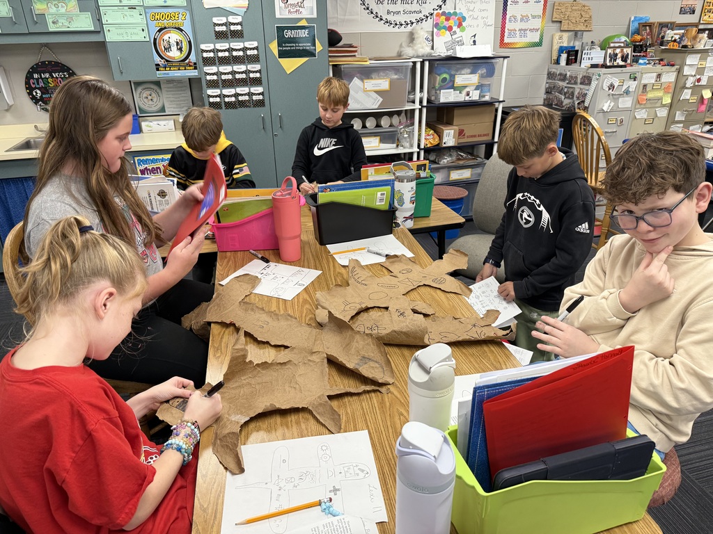 Group of kids sitting at a table working on designs made out of paper bags with drawings on them that resemble buffalo hides.