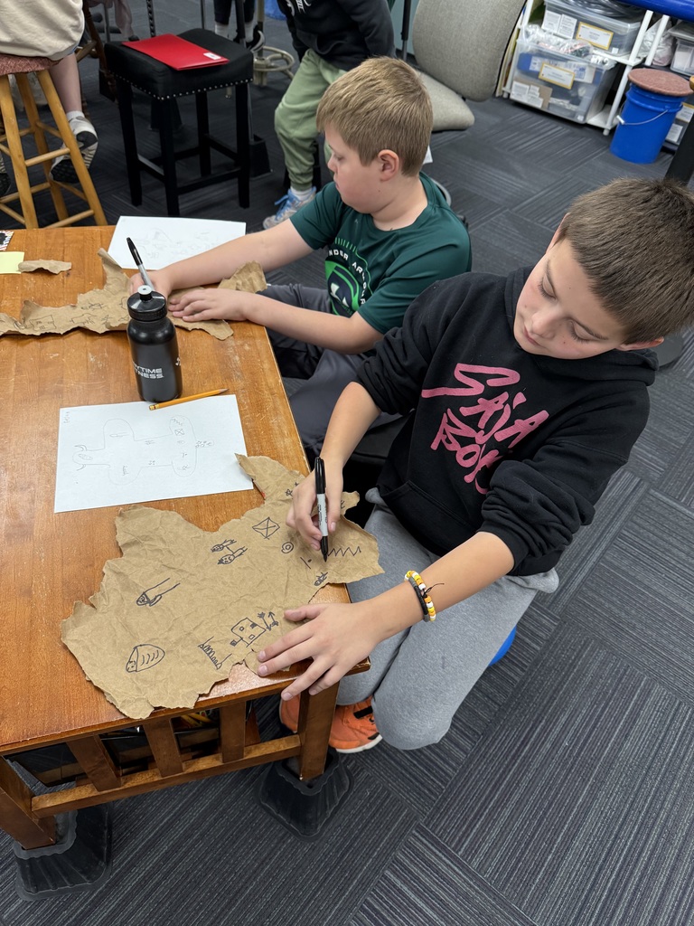 Two boys making designs made out of paper bags with drawings on them that resemble buffalo hides.