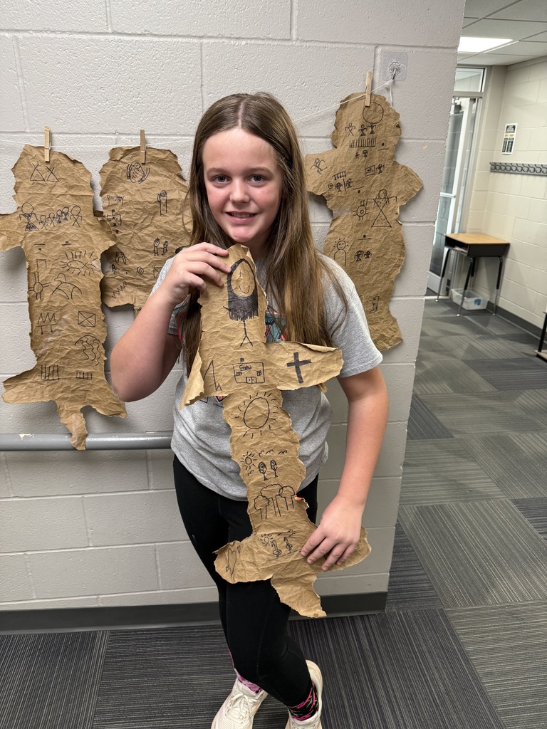 A girl holding a design made out of paper bags with drawings on them that resemble buffalo hides.