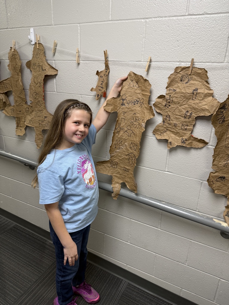 A girl holding a design made out of paper bags with drawings on them that resemble buffalo hides.