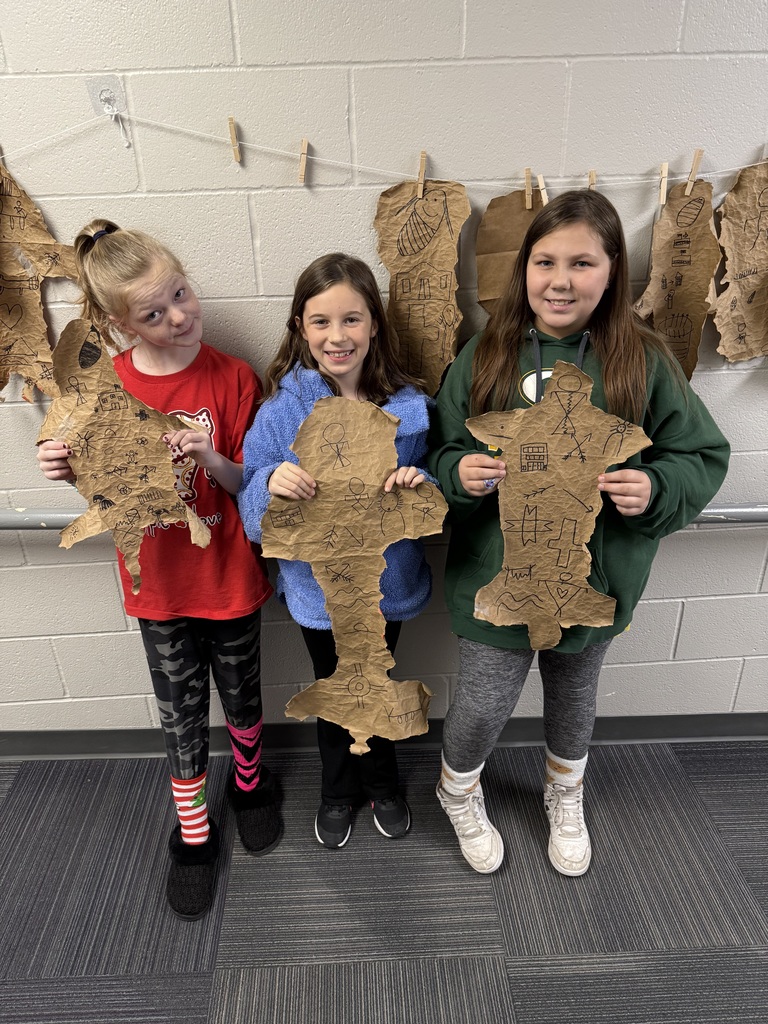 Three girls holding designs made out of paper bags with drawings on them that resemble buffalo hides.
