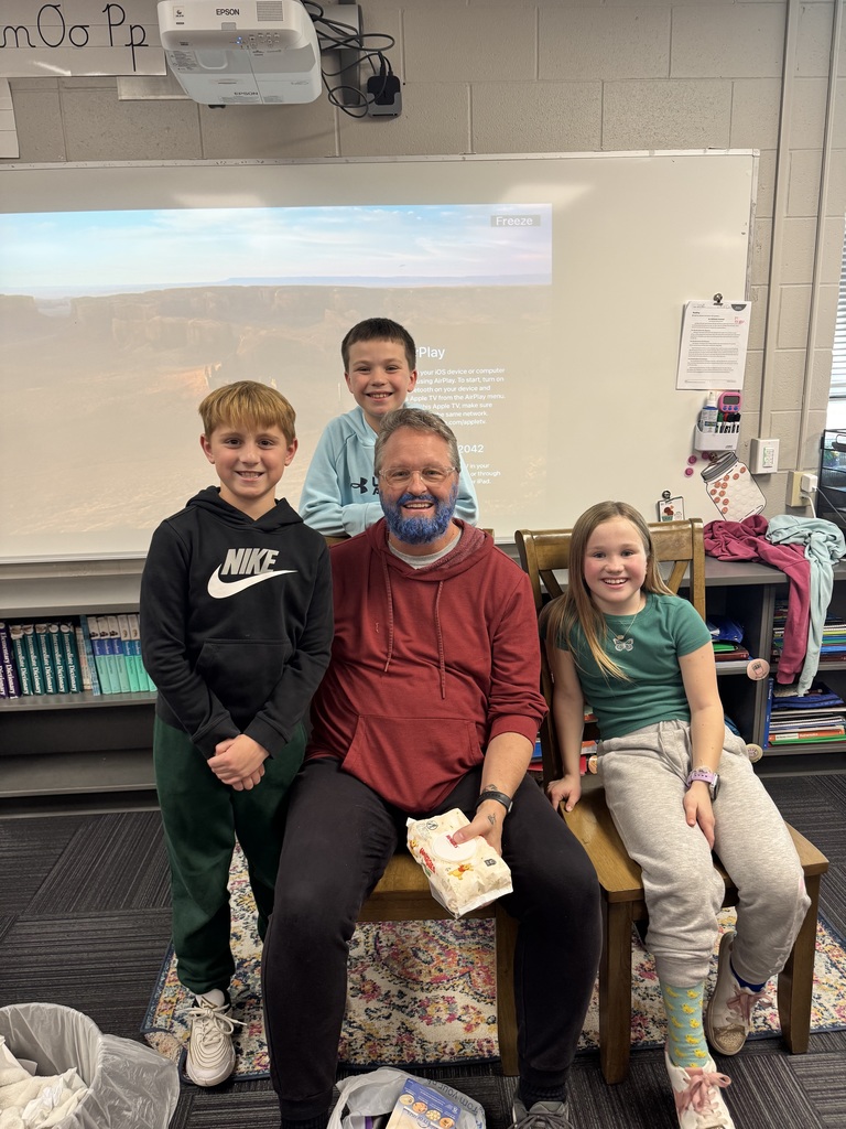 Man with a blue beard sitting on a chair surrounded by 3 kids.