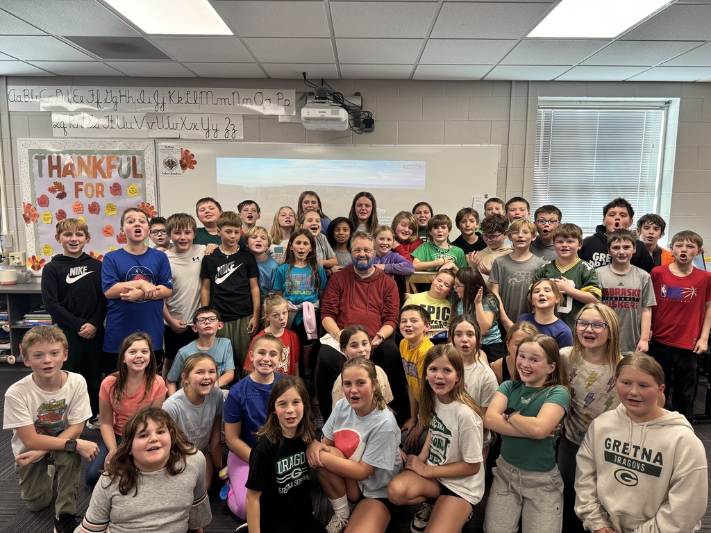 Group of students posing for a photo by a man sitting in a chair with a blue beard.