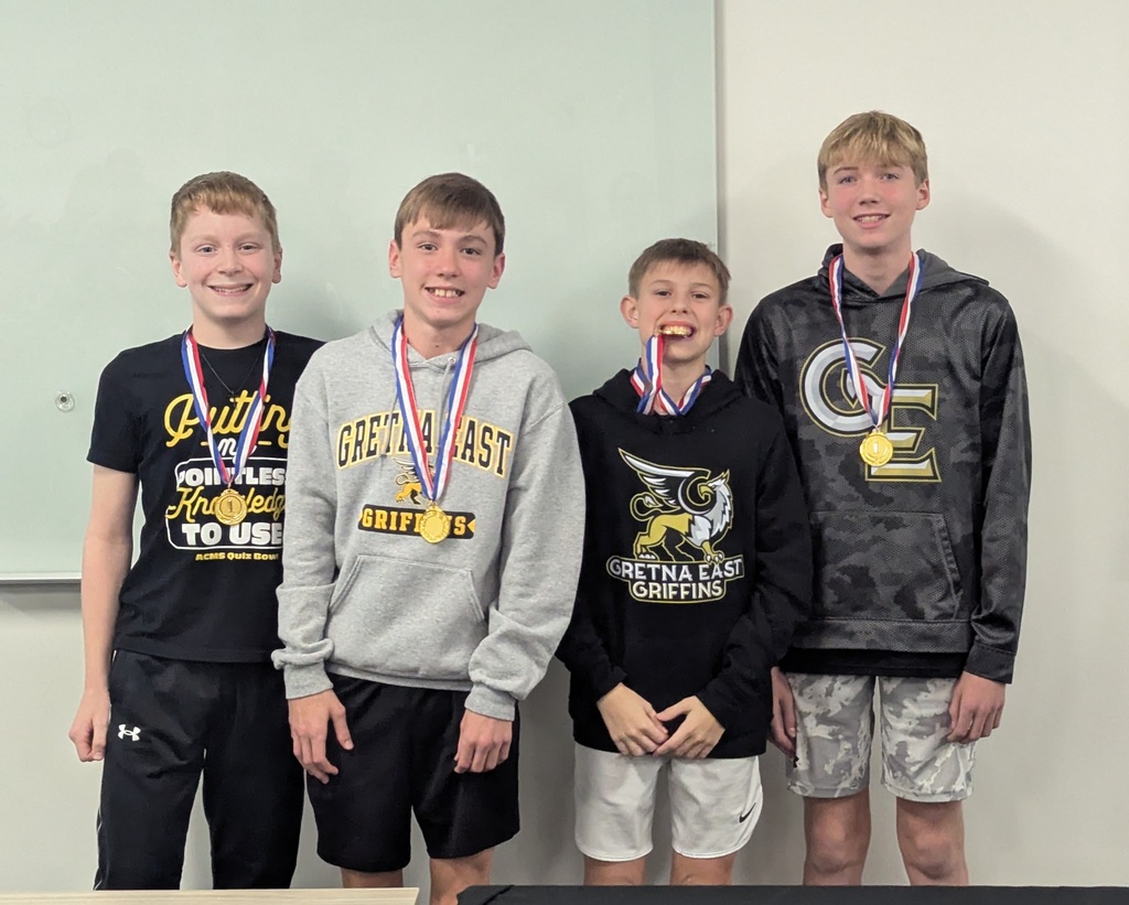 Photo of four students lined up wearing gold medals from their competition. One student is holding his medal between his teeth.