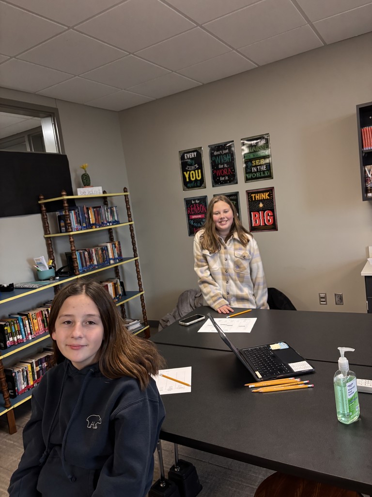 Photo of two students sitting at a table looking at the camera smiling.