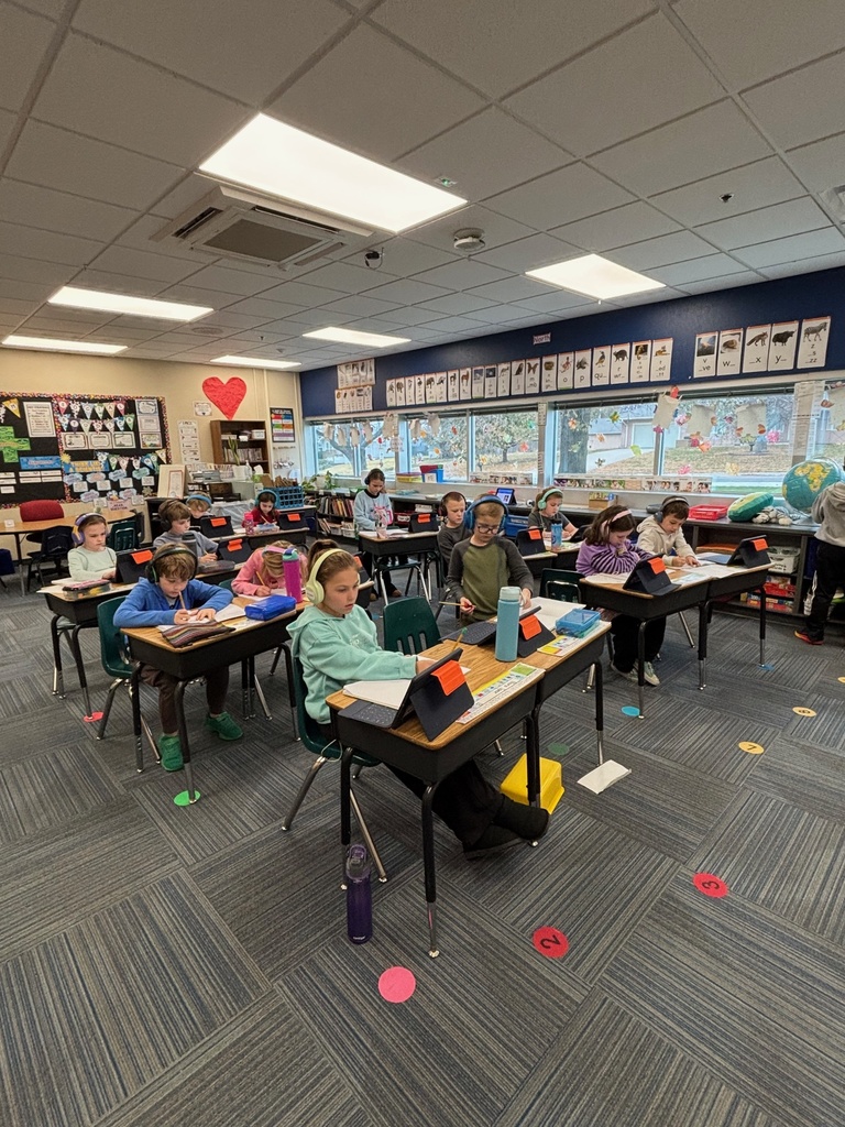 Group of 2nd graders sitting at their desks working with their headphones on and working on their iPads.