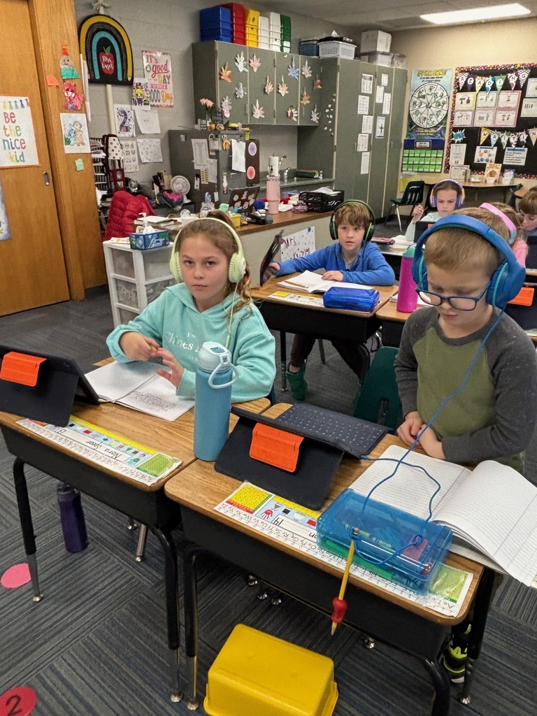 Group of 2nd graders sitting at their desks working with their headphones on and working on their iPads.