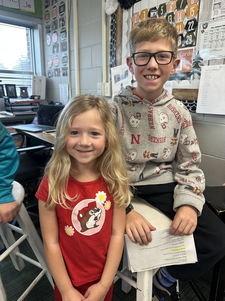 A boy sits on a stool while smiling next to a younger girl who is standing next to him.