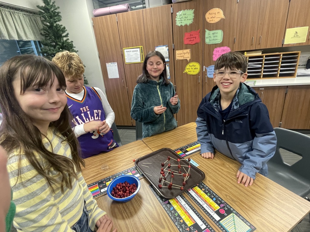Four students gather around a table smiling and build a tower using cranberries. 