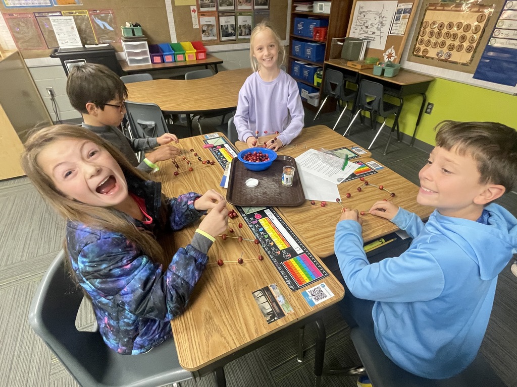 Four students gather around a table smiling and build a tower using cranberries. 
