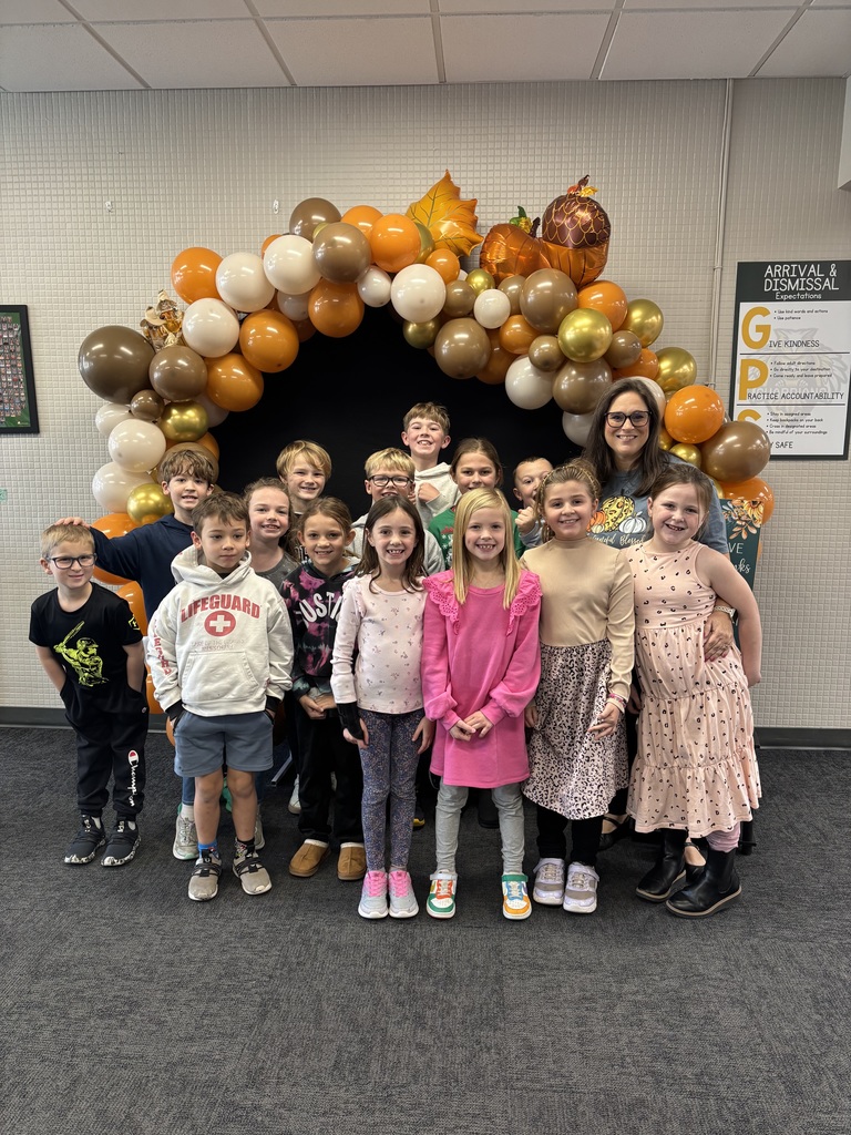 Group of students and their teacher standing around a balloon archway decorated for Thanksgiving!
