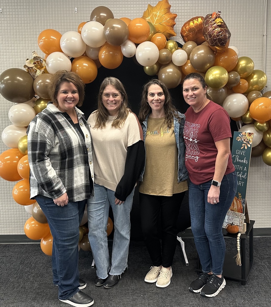 4 women standing around an arch made of Thanksgiving colored balloons.