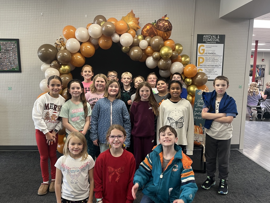 Group of students, some kneeling and some standing in front of an arch created out of Thanksgiving colored balloons.
