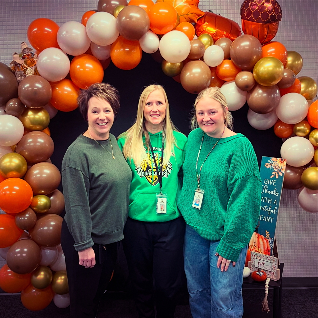 Three women standing in front of an arch made out of Thanksgiving colored balloons.