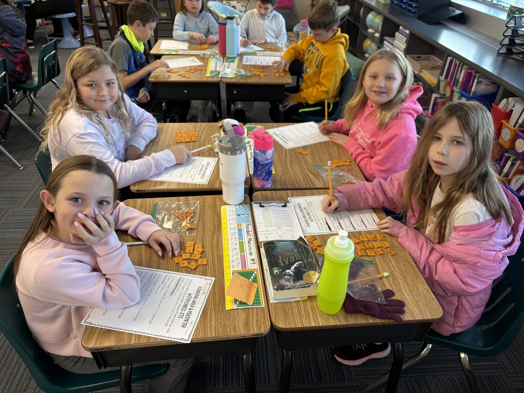Group of kids sitting at desks with a paper in front of them and cheese its as well doing a math activity.