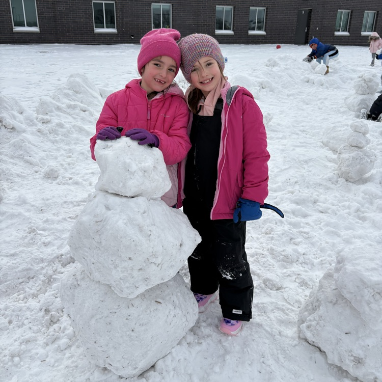 two girls in pink coats are building a snowman