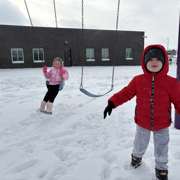 a girl in pink winter gear is on the swings and a boy in a red coat is smiling