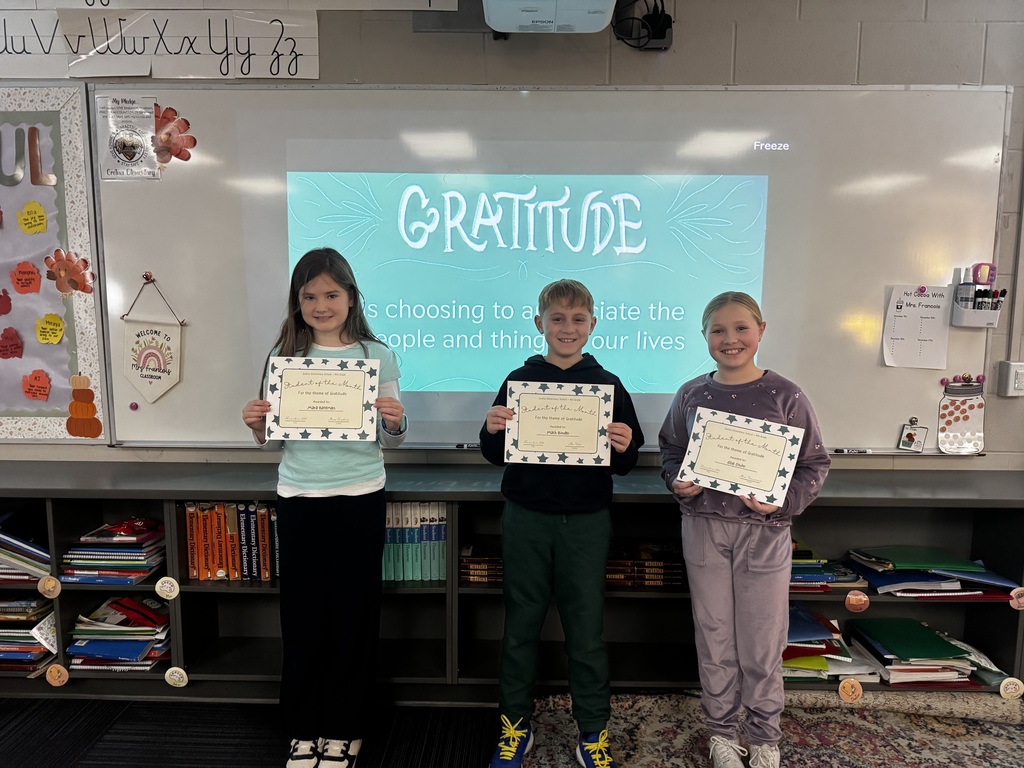 Three students standing in front of a whiteboard that says "Gratitude" while holding certificates.
