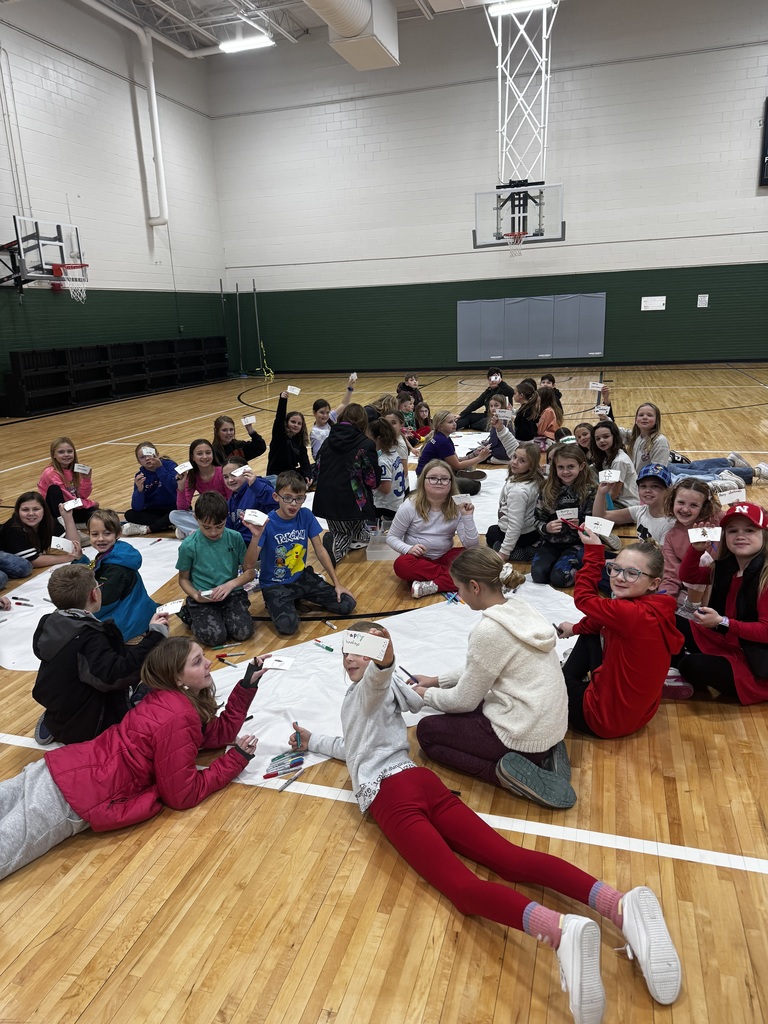 Group of students sitting and laying on a gym floor working on an art activity.