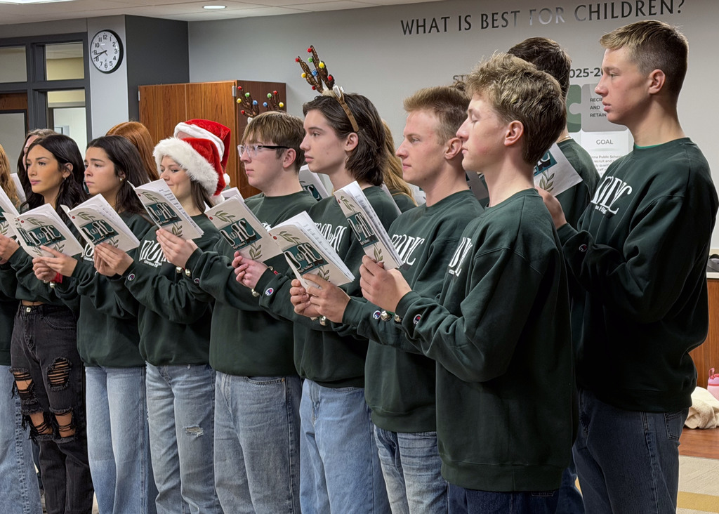 students singing in the board room with sheet music and some with reindeer antlers