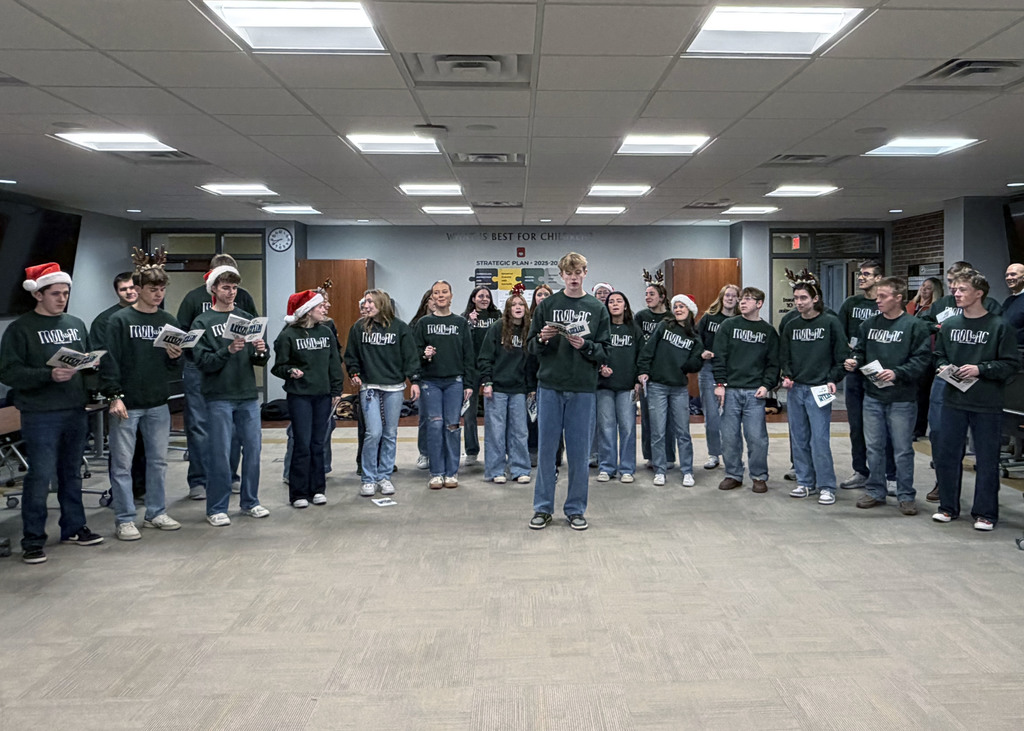 Large group of singers in board room singing with sheet music and dancing