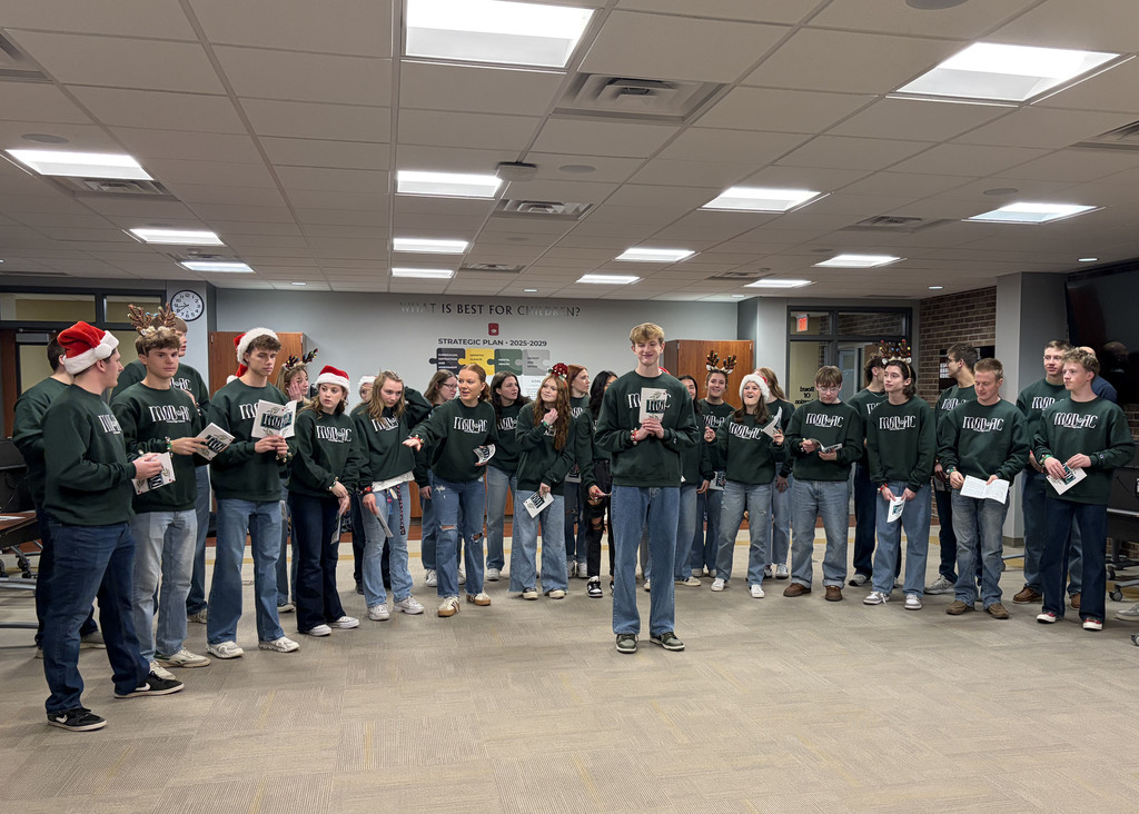 Large group of singers in board room performing with santa hats and reindeer antlers