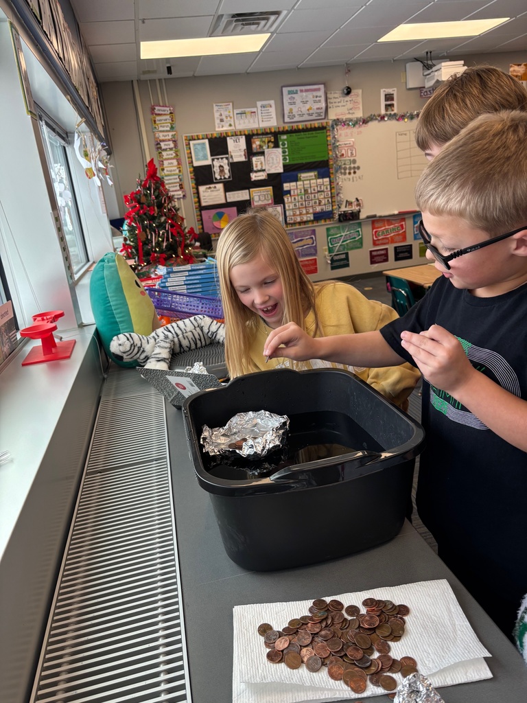Three students standing around a counter with a black tub present with aluminum foil and pennies.