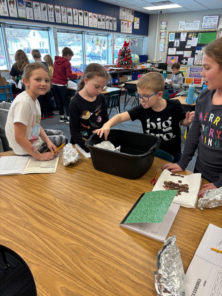 Four students standing around a table with a black tub present with aluminum foil and pennies.