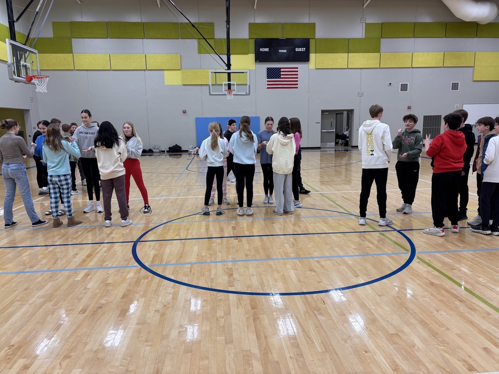 Photo of several pairs of students standing around the gym playing rock, paper, scissors.