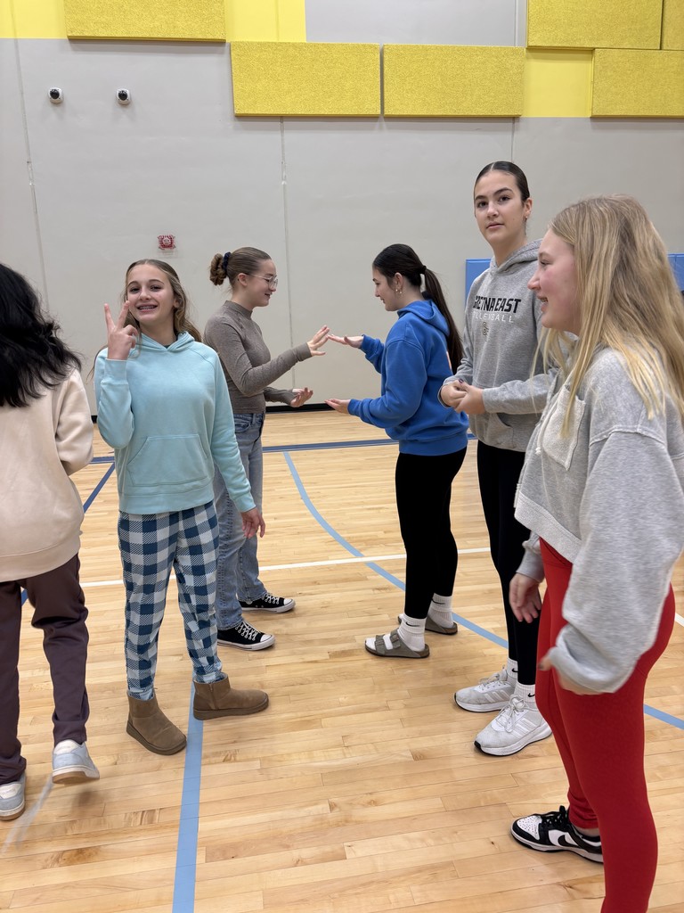 Photo of two female students battling in rock, paper, scissors. Other female students are gathered around. Some are watching the battle and others are looking at the camera.