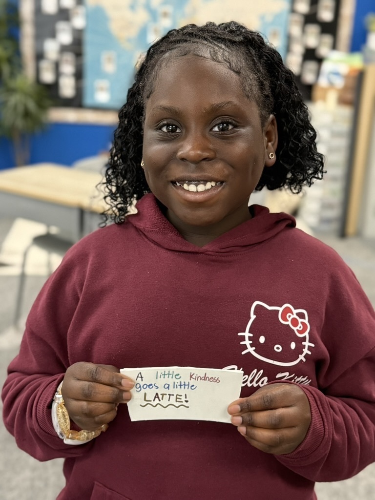 A student holding her decorated coffee sleeve that says "A little kindness goes a latte!