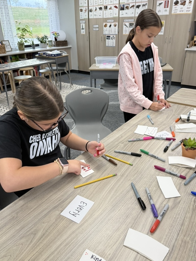two student at a table decorating coffee sleeves for kindness