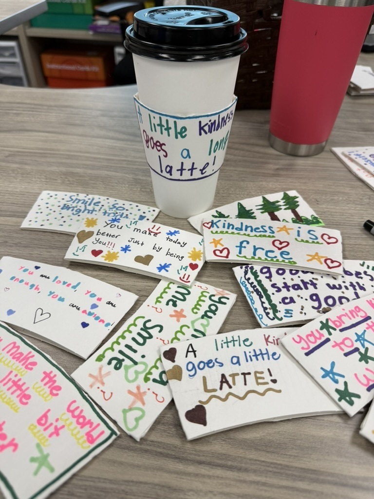 a classroom table full of decorated coffee sleeves.