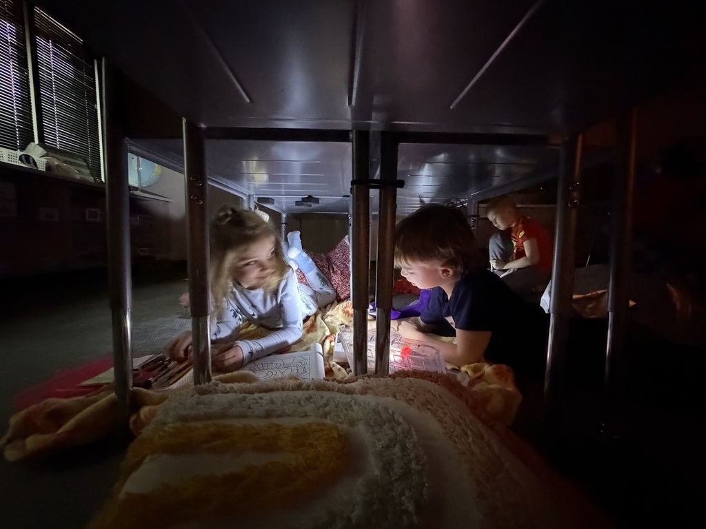 students under desks using flashlights to work.
