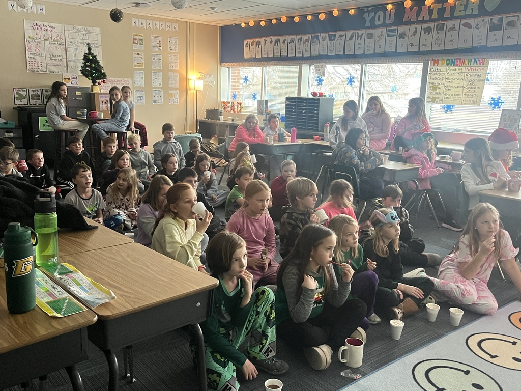 Group of students sitting in a classroom, some on the floor and some in chairs eating items from styrofoam cups.