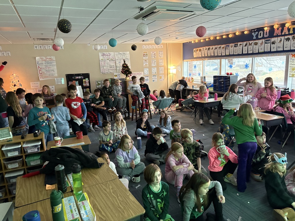 Large group of students in a room, some sitting on the floor while others are sitting on chairs or sitting on desks.