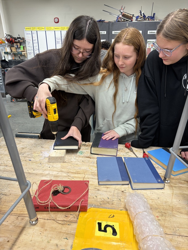 Photo of three female students working together to drill holes into their books.