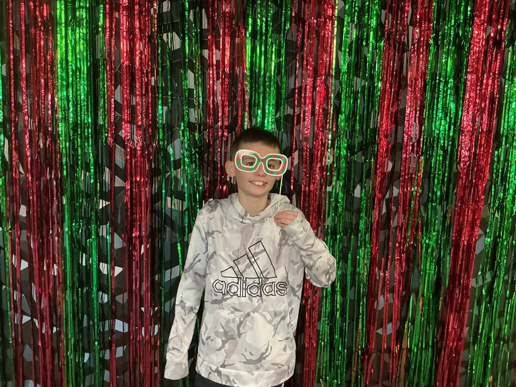 Photo of a male student standing in front of a green and red backdrop holding holiday-themed glasses to his face.