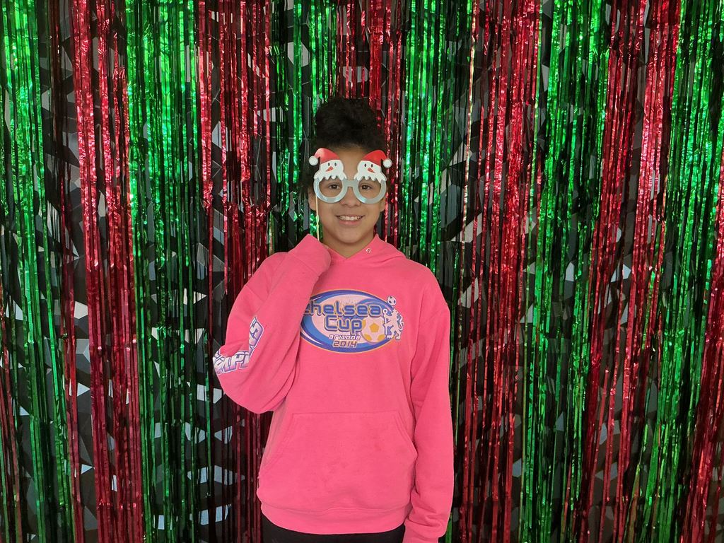 Photo of a female student standing in front of a green and red backdrop holding holiday-themed glasses to her face.