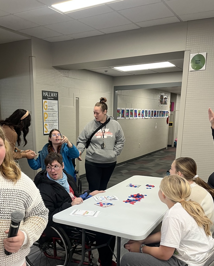 Group of students and adults sitting at a white table playing bingo with red and blue tiles.